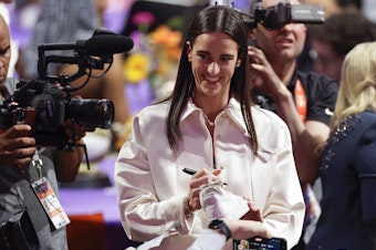 caption: Caitlin Clark, pictured autographing sneakers before the WNBA draft last Monday, is helping drive demand for the league's ticket sales and TV coverage.