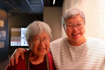 caption: Sisters Alice Hikido (left) and Mary Abo (right) stand for a photo in front of a new Washington State Fairgrounds memorial wall honoring the Japanese Americans who were once incarcerated there.