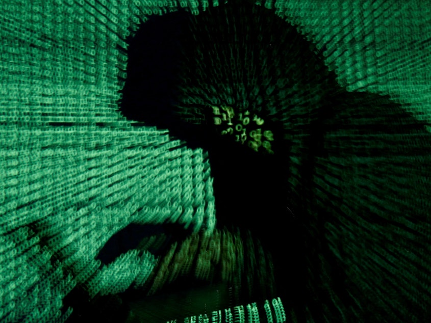 A man holds a laptop computer as cyber code is projected on him.