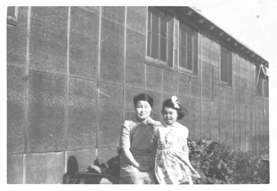 caption: Mary Abo, age 4, and her mother, Nobu Tanaka, in front of a barrack at the Minidoka, Idaho prison camp, circa 1944.