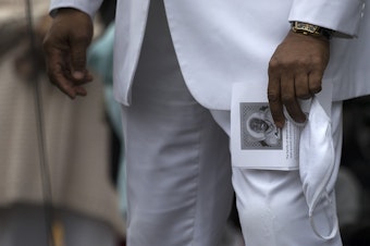 caption: Reverend Dr. Leslie Braxton, a pastor at New Beginnings Christian Fellowship holds a piece of paper with an image of Manuel Ellis on it along with a mask, following a silent march honoring the 33-year-old musician and father of two who was killed by Tacoma police one year ago, on Sunday, February 28, 2021, at People's Park in Tacoma. "He was literally lynched on the pavement," said Reverend Braxton. "We the people demand that justice be served."