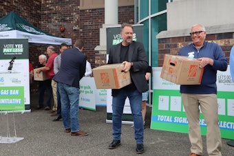 caption: Building Industry Association of Washington executive director Greg Lane (pictured right) and Let's Go Washington founder Brian Heywood (center right) help turn in boxes of signatures supporting I-2066, the initiative focused on protecting natural gas access, at the Secretary of State's office in Tumwater Tuesday, July 2, 2024.