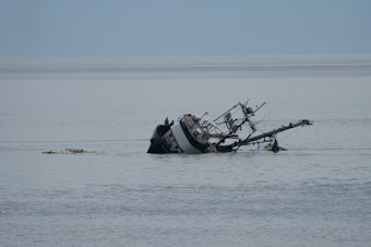 caption: Members of the crew stand near the starboard rail as the Aleutian Isle sinks off San Juan Island on Aug. 14, 2022.