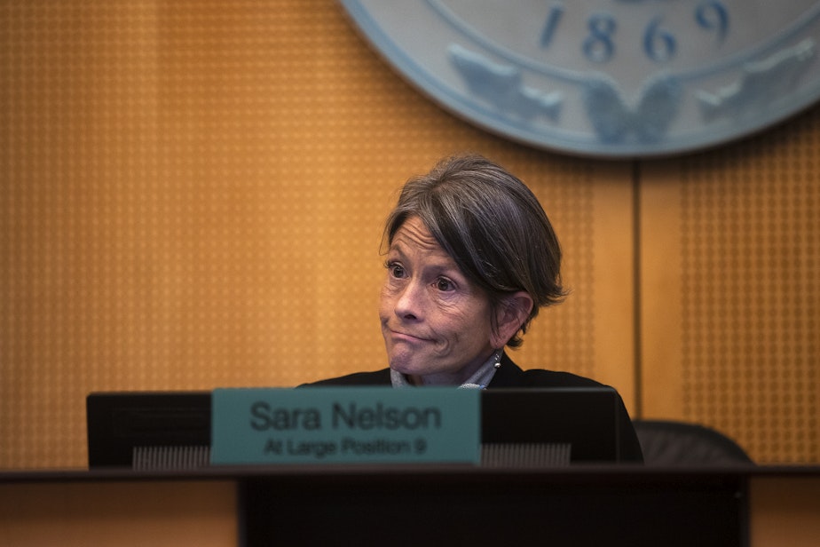 caption: Seattle City Council President Sara Nelson reacts during the public comment period of a city council meeting on Tuesday, Feb. 27, 2024, at Seattle City Hall. Asylum seekers once housed at the Sleep Inn in SeaTac, marched to Seattle City Hall along with activists, mutual aid organizations and allies to ask for assistance with housing.   