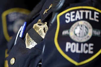 caption: FILE: A black band is drawn across the badge of Seattle Police Deputy Chief Carmen Best as she stands nearby during a news conference on Friday, July 8, 2016, in Seattle. 