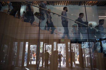 caption: Amazon employees and their parents are reflected leaving the Day 1 Building during Amazon's bring your parents to work day on Friday, September 15, 2017, in Seattle.