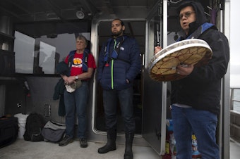 caption: From left, Kurt Russo and Tony Hillaire listen as Lawrence Solomon, right, sings the Lummi National Anthem before a ceremonial feeding where one live chinook salmon was released into the water, aboard King County Research Vessel SoundGuardian on Wednesday, April 10, 2019, near Henry Island.