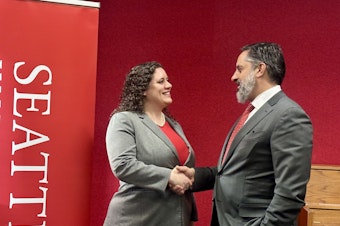 caption: Emily Parkhurst, Cornish College of the Arts' interim president, and Seattle University President Eduardo Peñalver shake hands as they pose for a photo December 5, 2024. The two private colleges announced their intent to merge.