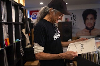 caption: Retiring KEXP DJ Kevin Cole holds a signed acetate Prince record in his home studio on Monday, July 8, 2024, in Seattle. 