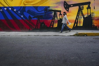 caption: A man walks past a mural featuring oil pumps and wells in Caracas, Venezuela, as the country faces the prospect of the U.S. reimposing oil sanctions.