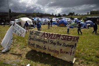 caption: Asylum seekers play with a soccer ball while awaiting a possible sweep of their new encampment location, in front of an empty Econo Lodge on Tuesday, June 4, 2024, in Kent. 