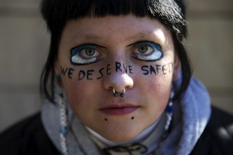 caption: E.O Franklin-Bihary was a sophomore at Ingraham High School when a student was shot and killed in the school. They're portrayed with the words "we deserve safety" painted across their face during a student walkout to protest gun violence in schools on Monday, Nov. 14, 2022, at Seattle City Hall. 