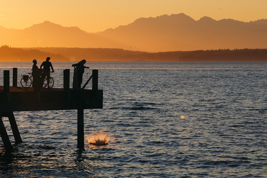 caption: A crab trap splashes down off a pier near Alki Beach as the sun sets, September 1, 2021.
