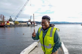 caption: Ashley Townes stands at the edge of Lake Washington where logs are being arranged in the water to help promote aquatic plant growth, enhance water quality, and provide habitat for animals.