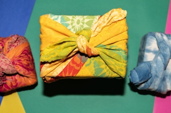 Photograph of three gifts wrapped in fabric photographed from overhead against a colorful background.