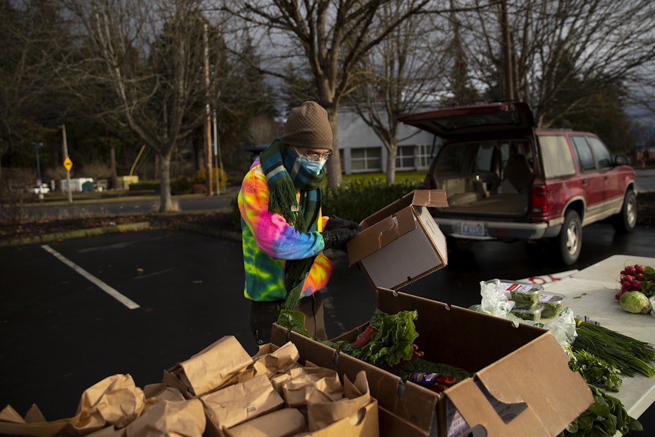 caption: Volunteer Carter Fuehr sets up produce ahead of a weekly food distribution event on Saturday, Dec. 10, 2022, in Bellingham. 