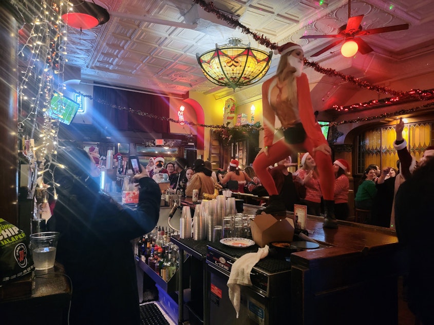 caption: Natalie Lacayo films a twerking Santa at Merchants Cafe & Saloon during SantaCon on December 7, 2024.