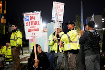 caption: Boeing employee Dianna Vu, 20, a grade 6 mechanic, holds a picket sign with coworkers after union members voted overwhelmingly to reject a contract offer and go on strike Friday, Sept. 13, 2024, outside the company's factory in Renton, Wash. 