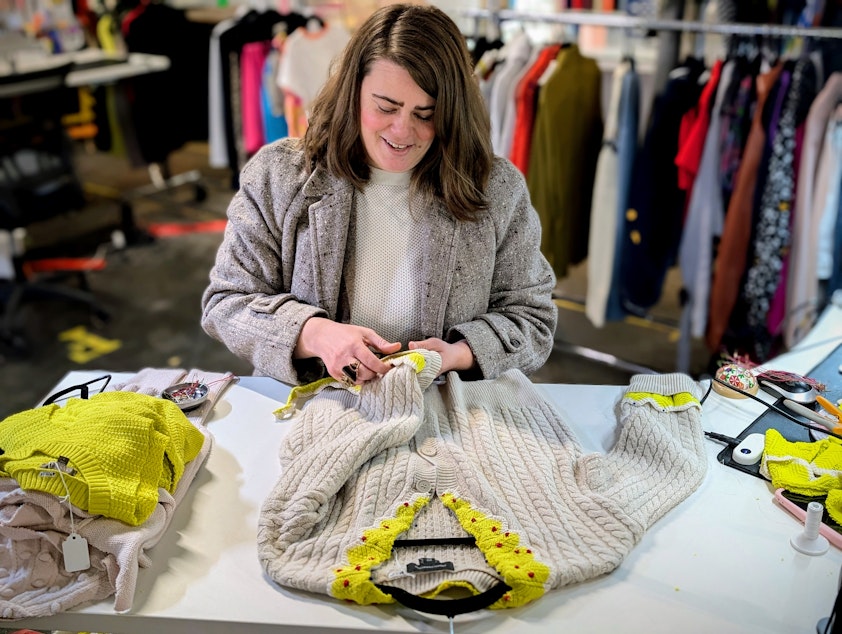 caption: Armoire's Sam Martin works on upcycling damaged garments into holiday sweaters.