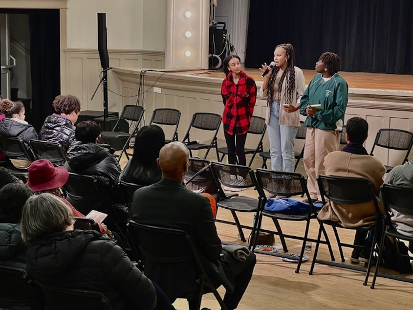 caption: Haben Haileslassie (left) stands next to Diana Muuru (center) and Mikayla Weary (right) at Washington Hall in Seattle's Central District. They are part of the Black Coffee Northwest Grounded youth program, and moderated a youth panel on public safety on Tuesday, Dec. 12, 2023.