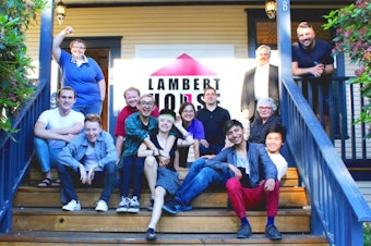 caption: People gather for a group photo on the steps of the Lambert House in Seattle, Washington. 