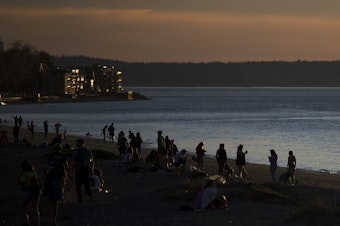 caption: People gather to watch the sunset on Tuesday, March 19, 2019, at Alki Beach Park in Seattle. 