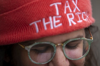 caption: Whitney Kahn attends an "All Together for Seattle Schools" rally wearing a hat that reads "tax the rich" ahead of a school closures meeting on Tuesday, May 28, 2024, at Roosevelt High School in Seattle. 