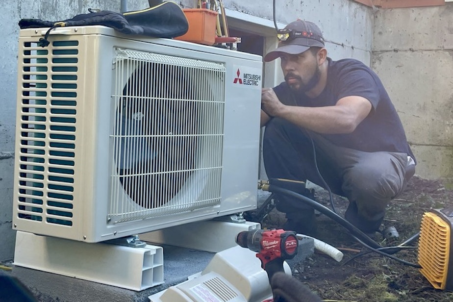 caption: CM Heating technician Saul Benitez installs an electric heat pump in Shoreline, Washington, on July 28, 2023.