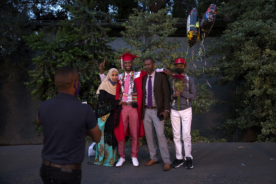 caption: Tuji Ahmed poses for a picture with his family members after graduating from Cleveland Stem High School in-person, on Tuesday, June 15, 2021, at Memorial Stadium in Seattle.