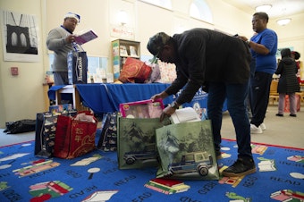 caption: Rogers Greene, a family support worker at Dunlap Elementary School, sorts gifts for students on Friday, December 20, 2024, at Dunlap Elementary School in Seattle.