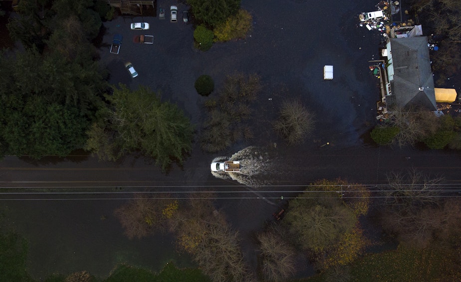 caption: A truck drives through a flooded stretch of Old Day Creek Road on Tuesday, November 16, 2021, in Clear Lake, Washington.