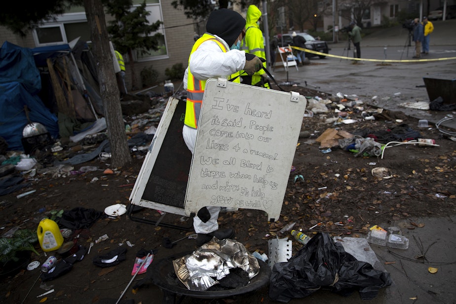 caption: A Seattle Parks and Recreation employee discards a hand written sign that was left behind after unhoused community members were swept from the Ballard Commons Park on Tuesday, December 7, 2021, in Seattle. 