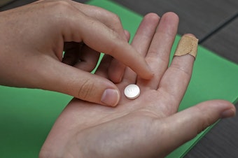 caption: A patient prepares to take the first of two combination pills, mifepristone, for a medication abortion during a visit to a clinic in Kansas City, Kan., on Oct. 12, 2022.