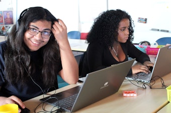 caption: Daniel Colindres-Flores smiles as he works on editing audio next to Rediet Giday at RadioActive Youth Media.