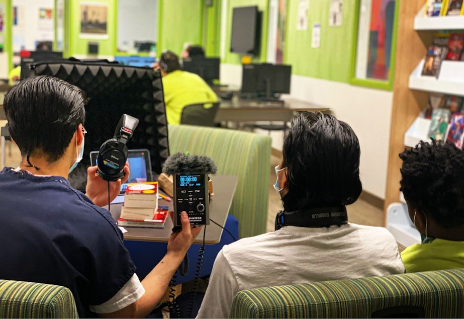 caption: Three teens get ready to record an interview in the library at the Judge Patricia H. Clark Children and Family Justice Center during a RadioActive podcasting workshop on April 15, 2021.