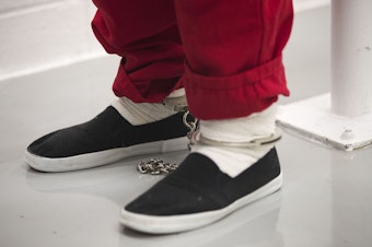 caption: A detainee's legs are shown chained together in the intake holding area on Tuesday, September 10, 2019, at the Northwest Detention Center, recently renamed the Northwest ICE Processing Center, in Tacoma.