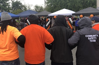 caption: People stand in the rain and link arms at an event for National Gun Violence Awareness Day in Skyway, Washington on June 3, 2022.