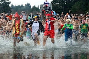 caption: Soren Johnson (left), Dylan McMaster (middle), and Bryan Johnson (right) run into Lake Washington Monday as part of the annual Polar Bear Plunge.