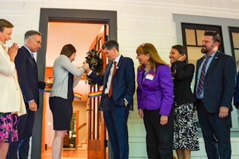 caption: Lindsay Church, in the suit on the right side of the doorway, is joined by loved ones, local, state, and federal officials marking the opening of a new transitional housing program for LGBTQ+ veterans. Also in attendance were representatives from Veterans Affairs, King County Executive Dow Constantine, and Congressmembers Pramila Jayapal and Adam Smith.