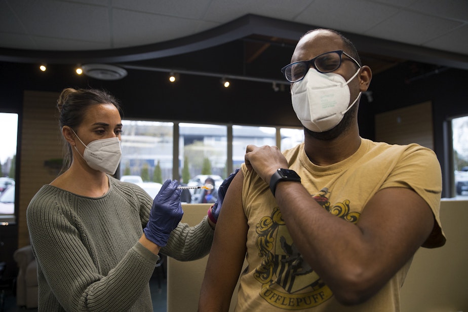 caption: Volunteer registered nurse Amy Rioux, left, administers a Covid-19 vaccine for Teddy Haile of Seattle, right, on Wednesday, April 7, 2021, at Island Drug in Oak Harbor. 