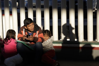 caption: A migrant and his children wait to hear if their number is called to apply for asylum in the United States, at the border in Tijuana, Mexico.