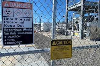 caption: A gate and signs stand guard at one of the Hanford site’s tank farms.