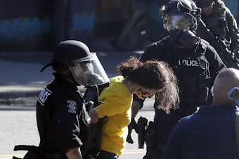 caption: Police arrest a person wearing a yellow shirt an armband that reads "Mom," Saturday, July 25, 2020, during a Black Lives Matter protest near Seattle Central Community College in Seattle. A large group of protesters were marching Saturday in Seattle in support of Black Lives Matter and against police brutality and racial injustice.