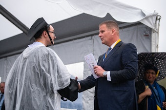 caption: Robert Hale gives an envelope with cash to a graduating UMass Dartmouth student at last week's commencement. Each of the 1,200 graduates received $1,000 onstage, half to keep and half to donate.