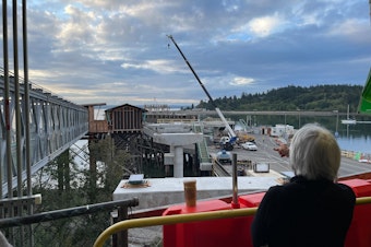 caption: A ferry passenger watches construction on a new walkway that is being built at the Bainbridge Island ferry terminal on Sept. 7, 2023.