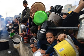 caption: Palestinian children wait to collect food at a donation point in a refugee camp in Rafah in the southern Gaza Strip on December 23, 2023.