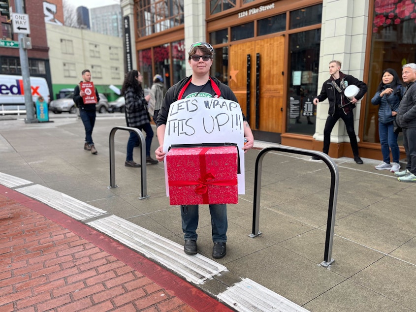 caption: Starbucks barista Mari Cosgrove strikes Friday in front of the Pike Street Starbucks Reserve Roastery in Seattle. 