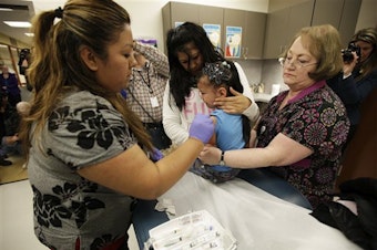 caption: Nurses Fatima Guillen, left, and Fran Wendt, right, give Kimberly Magdeleno, 4, a Tdap whooping cough booster shot in Tacoma, Washington in 2012.