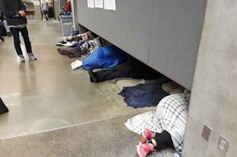 caption: People sleep while waiting in line early Thursday at the Seattle Center's Fisher Pavilion for a free health clinic to open.