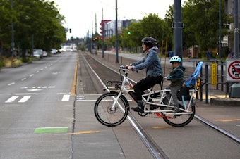 caption: Clara Cantor crosses Martin Luther King Jr. Way South while riding along South Kenyon Street with her 4-year-old son, on Friday, June 14, 2024, in Seattle. 